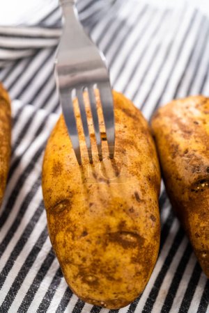 Téléchargez les photos : Pressure Cooker Baked Potatoes. Poking raw potatoes with a fork to prepare baked potatoes. - en image libre de droit