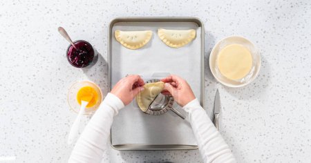 Téléchargez les photos : Pose plate. Remplissage de pâte empanada avec garniture tarte aux myrtilles pour faire des empanadas sucrés aux myrtilles. - en image libre de droit