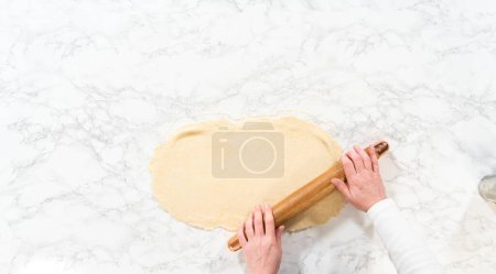 Foto de Acostado. Rolling bread tough con un rodillo francés para hornear pasteles de canela sin levadura. - Imagen libre de derechos