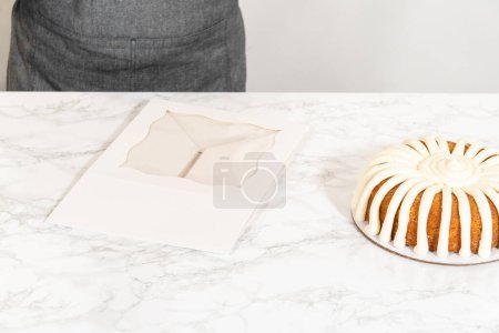 Téléchargez les photos : Le gâteau Bundt aux carottes est soigneusement emballé dans une boîte à gâteau Bundt en papier blanc, prêt à offrir ou à partager. - en image libre de droit