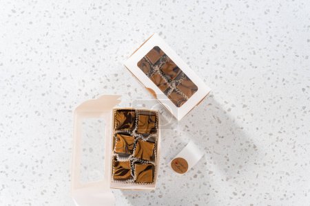 Téléchargez les photos : Pose plate. Emballage de caramel au chocolat fait maison avec du beurre d'arachide tourbillonner dans une boîte cadeau blanche. - en image libre de droit
