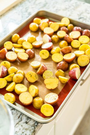 Photo for In a modern kitchen, an array of halved, multicolored marble potatoes are arranged on a baking pan lined with a silicone liner. The roasting process infuses the kitchen with a mouthwatering aroma - Royalty Free Image
