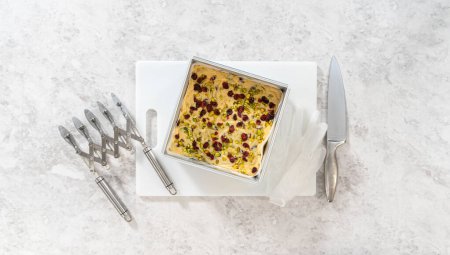 Photo for Flat lay. Removing cranberry pistachio fudge from a square cheesecake pan lined with parchment. - Royalty Free Image