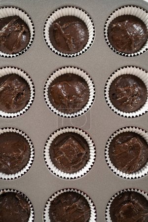 Photo for Scooping cake batter with dough scoop into cupcake foil liners to bake chocolate peppermint cupcakes. - Royalty Free Image
