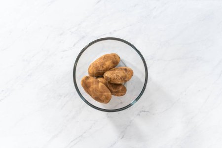Photo for Flat lay. Pressure Cooker Baked Potatoes. Washing raw potatoes in a glass mixing bowl with water. - Royalty Free Image