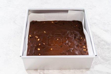 Photo for Filling square cheesecake pan lined with parchment paper with fudge mixture to prepare chocolate hazelnut fudge. - Royalty Free Image
