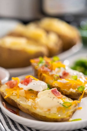 Téléchargez les photos : Pressure Cooker Baked Potatoes. Garnished large baked potatoes with butter, sour cream, cheese, and bacon bits on a white plate. - en image libre de droit