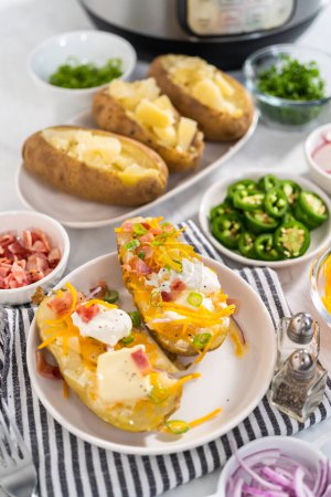Photo for Pressure Cooker Baked Potatoes. Garnished large baked potatoes with butter, sour cream, cheese, and bacon bits on a white plate. - Royalty Free Image