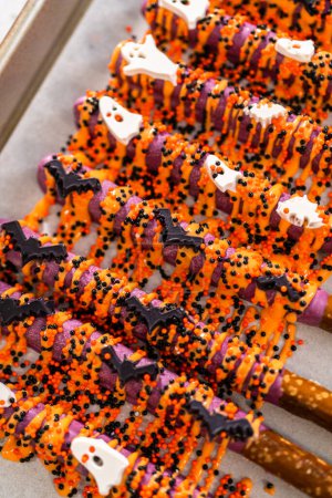 Téléchargez les photos : Tremper les tiges de bretzel dans du chocolat fondu pour faire des tiges de bretzel recouvertes de chocolat Halloween. - en image libre de droit