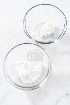 Téléchargez les photos : Ingrédients mesurés dans de petits bols à mélanger en verre pour faire de la poussière de sucre en poudre. - en image libre de droit