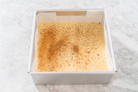 Photo for Pouring fudge mixture into the square cheesecake pan lined with parchment paper to prepare eggnog fudge. - Royalty Free Image