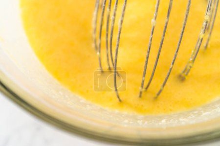 Foto de Mezclar ingredientes húmedos en un tazón de vidrio grande para hornear pastel de paquete de arándanos limón. - Imagen libre de derechos