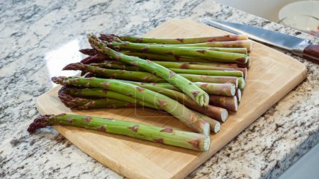 Photo for Large organic asparagus stalks are being sliced in a modern white kitchen, in preparation for steaming. - Royalty Free Image