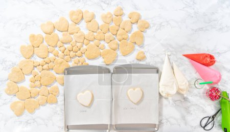 Photo for Flat lay. Decorating heart-shaped sugar cookies with pink and white royal icing for Valentines Day. - Royalty Free Image