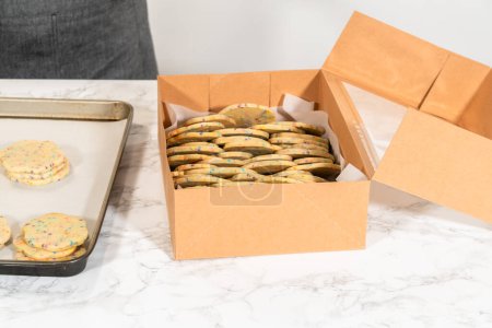 Téléchargez les photos : Avec précision, la femme arrange soigneusement les biscuits au sucre, remplis de saupoudres mélangées à la pâte, dans une boîte en papier brun rustique. - en image libre de droit