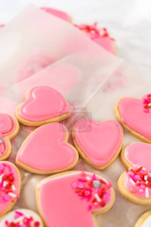 Foto de Almacenamiento de galletas de azúcar en forma de corazón con glaseado real rosa y blanco en un recipiente de plástico grande. - Imagen libre de derechos