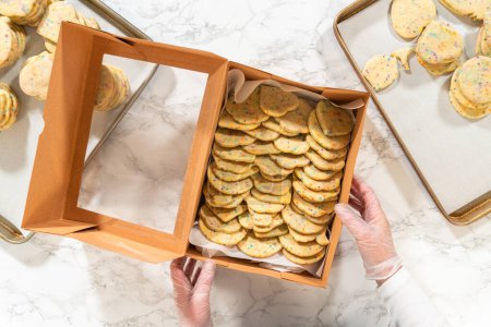 Photo for Flat lay. With precision, the woman is carefully arranging the sugar cookies, filled with dough-mixed sprinkles, into a rustic brown paper box. - Royalty Free Image