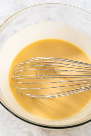 Foto de Mezclar ingredientes húmedos y secos con un batidor de mano en un tazón de vidrio para hornear un pastel de zanahoria con glaseado de queso crema. - Imagen libre de derechos