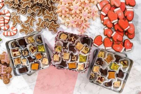 Photo for Flat lay. Packaging a homemade variety of fudge and gingerbread cookies for Christmas food gifts into tin boxes. - Royalty Free Image