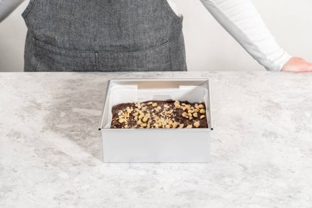 Foto de Filling square cheesecake pan lined with parchment paper with fudge mixture to prepare chocolate hazelnut fudge. - Imagen libre de derechos