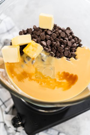 Photo for Melting white chocolate chips and other ingredients in a glass mixing bowl over boiling water to prepare chocolate macadamia fudge. - Royalty Free Image