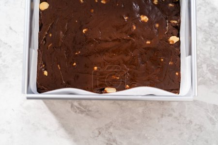 Téléchargez les photos : Poêle à gâteau au fromage carrée garnie de papier sulfurisé avec mélange de caramel pour préparer du caramel macadamia au chocolat. - en image libre de droit