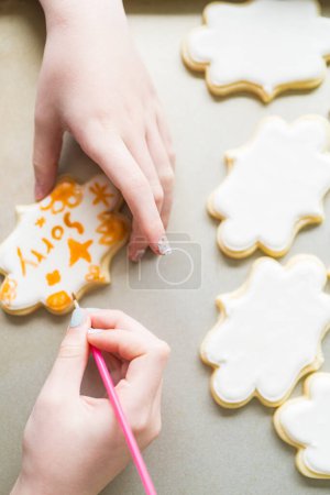 Téléchargez les photos : Une scène chaleureuse d'une petite fille écrivant avec soin Désolé sur les biscuits au sucre avec colorant alimentaire, les biscuits magnifiquement inondés de glaçage royal blanc. - en image libre de droit