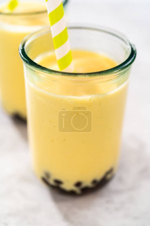 Téléchargez les photos : Freshly made mango boba smoothie in a drinking glass with a paper straw. - en image libre de droit