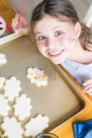 Foto de Una escena conmovedora de una niña pequeña escribiendo cuidadosamente Lo sentimos en las galletas de azúcar con colorante de alimentos, las galletas bellamente inundadas con glaseado real blanco. - Imagen libre de derechos