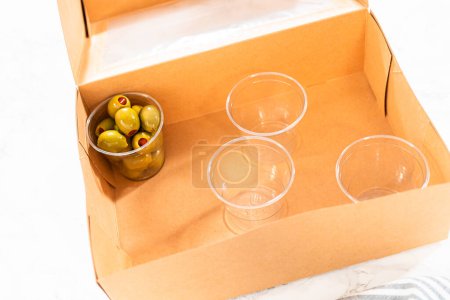 Photo for In the process of assembling, a woman expertly curates this charcuterie box, showcasing sliced meat, cheese, crackers, and grapes, all neatly arranged and packaged in a brown gifting box. - Royalty Free Image