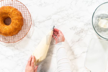 Téléchargez les photos : Le glaçage crémeux et délicieux au beurre de fromage à la crème est délicatement transféré dans un sac de tuyauterie, doté d'une pointe ronde en métal, prêt pour la décoration du gâteau Bundt aux carottes. - en image libre de droit