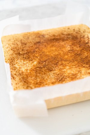 Téléchargez les photos : Enlever le caramel au lait de poule d'une poêle à gâteau au fromage carrée doublée de parchemin. - en image libre de droit