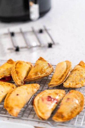 Téléchargez les photos : Empanadas de cerises douces fraîchement cuites dans la friteuse sur le comptoir de la cuisine. - en image libre de droit