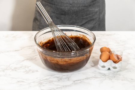 Foto de En el proceso de crear deliciosos cupcakes de chocolate, el primer paso consiste en mezclar meticulosamente los ingredientes en un tazón de vidrio para hacer la masa perfecta.. - Imagen libre de derechos