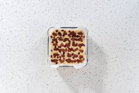 Photo for Flat lay. Pouring fudge mixture into the baking pan lined with parchment paper to prepare white chocolate cranberry pecan fudge. - Royalty Free Image