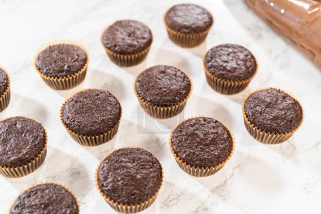 Téléchargez les photos : Cupcakes au chocolat fraîchement cuits sont prêts pour une transformation délicieuse car ils attendent un revêtement généreux de glaçage au chocolat riche et velouté. - en image libre de droit