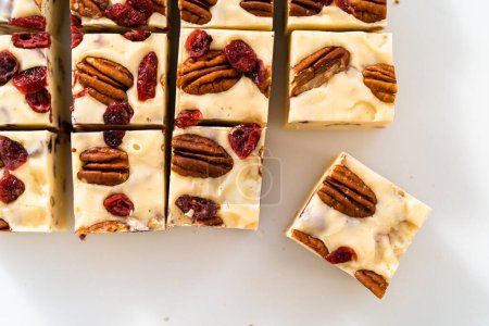 Foto de Corte de chocolate blanco dulce de nuez de arándano en trozos pequeños en una tabla de cortar blanca. - Imagen libre de derechos