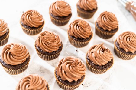 Téléchargez les photos : Des tourbillons délicats de glaçage au chocolat riche sont soigneusement pipés sur chaque cupcake au chocolat, créant un régal irrésistible. - en image libre de droit