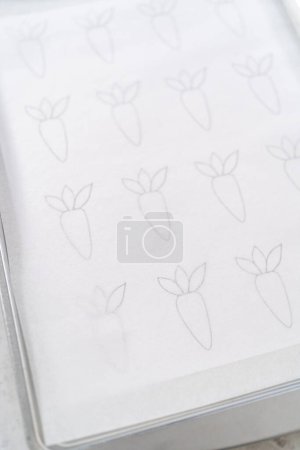 Photo for Piping melted chocolate from a piping bag over the parchment paper to make chocolate carrot cake toppers. - Royalty Free Image