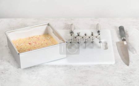 Foto de Extracción de caramelo fudge bastón de una sartén de pastel de queso cuadrado forrado con pergamino. - Imagen libre de derechos