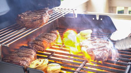 Photo for The outdoor two-burner gas grill is put to good use, sizzling with the sound and aroma of ribeye steaks and onion rings being perfectly cooked. - Royalty Free Image