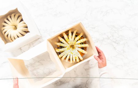 Photo for Flat lay. The freshly baked bundt cakes are carefully nestled into white paper boxes, preparing them for secure transportation while maintaining their delectable appearance. - Royalty Free Image