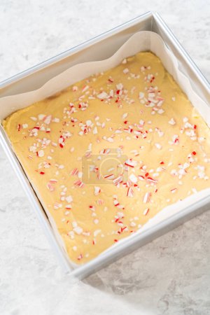 Foto de Llenado cuadrado de tarta de queso forrado con papel pergamino con mezcla de caramelo para preparar dulce de caña de azúcar. - Imagen libre de derechos