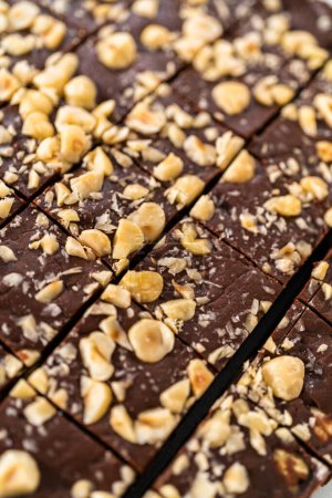 Photo for Cutting chocolate hazelnut fudge with a large kitchen knife into square pieces on a white cutting board. - Royalty Free Image