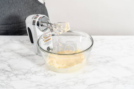 Téléchargez les photos : Mélanger les ingrédients avec un mélangeur à main dans un grand bol à mélanger pour faire cuire des mini cupcakes à la vanille avec ombre rose crème au beurre glaçage. - en image libre de droit