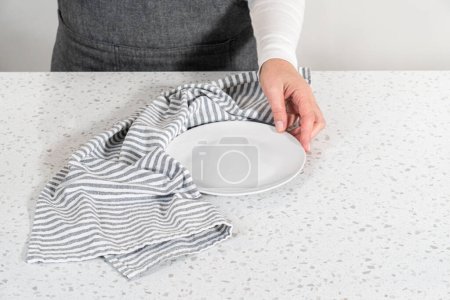 Téléchargez les photos : Vider une assiette blanche avec un torchon sur le comptoir de cuisine blanc. - en image libre de droit