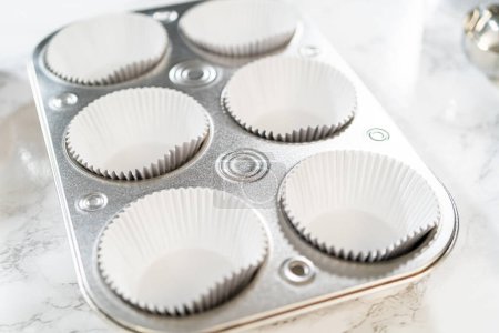 Téléchargez les photos : Les doublures en papier d'aluminium Cupcake sont méticuleusement remplies de chocolat et de pâte à la vanille, préparant le terrain pour la cuisson de cupcakes d'anniversaire délicieusement variés. - en image libre de droit