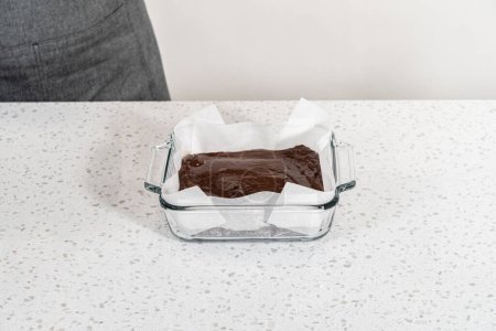 Téléchargez les photos : Verser le mélange de caramel dans le moule tapissé de papier sulfurisé pour préparer le caramel au chocolat avec tourbillon de beurre d'arachide. - en image libre de droit