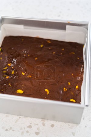Foto de Filling square cheesecake pan lined with parchment paper with fudge mixture to prepare chocolate pistachio fudge. - Imagen libre de derechos