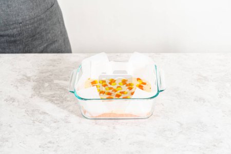 Téléchargez les photos : Removing candy corn fudge from a square glass baking pan lined with parchment. - en image libre de droit